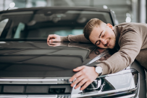 Hombre guapo joven abrazando un coche en una sala de exposición de automóviles