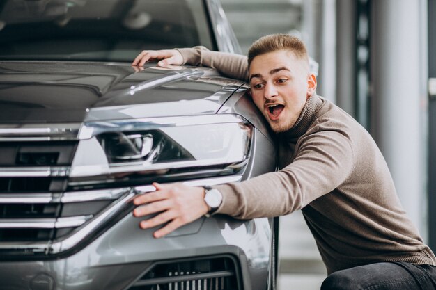 Hombre guapo joven abrazando un coche en una sala de exposición de automóviles