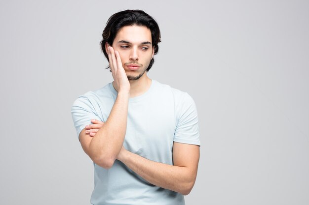 Hombre guapo joven aburrido manteniendo la mano en la cara mirando al lado aislado sobre fondo blanco con espacio de copia