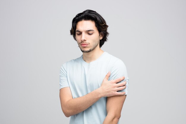 Hombre guapo joven adolorido manteniendo la mano en el brazo con los ojos cerrados aislado sobre fondo blanco con espacio de copia