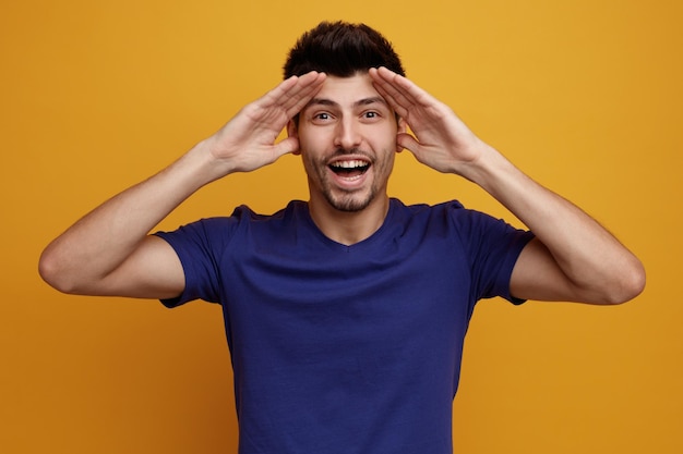 Foto gratuita hombre guapo joven alegre mirando a la cámara manteniendo las manos en la frente sobre fondo amarillo