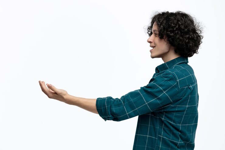 Foto gratuito hombre guapo joven alegre de pie en la vista de perfil mirando al lado estirando la mano aislado sobre fondo blanco.