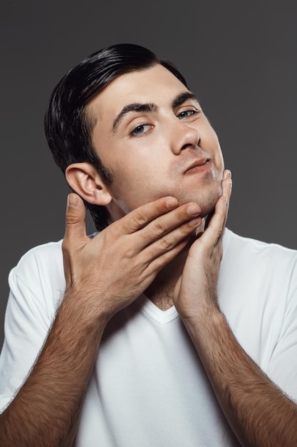 Hombre guapo joven aplicar crema para después del afeitado en la cara en gris