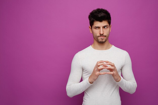 Hombre guapo joven astuto mirando al lado planeando algo malvado sobre fondo púrpura con espacio de copia