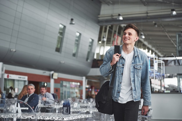 Hombre guapo joven con una bolsa en el hombro a toda prisa hacia el aeropuerto.