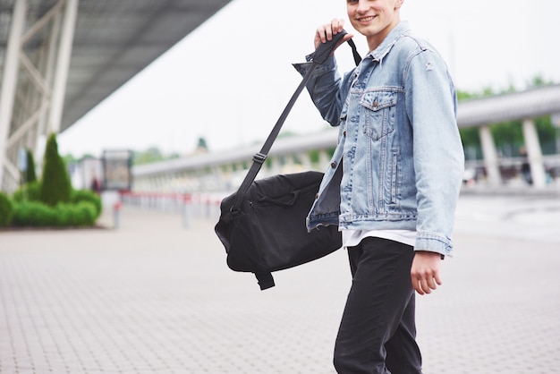 Hombre guapo joven con una bolsa en el hombro a toda prisa hacia el aeropuerto.