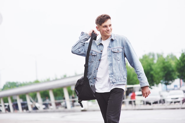 Hombre guapo joven con una bolsa en el hombro a toda prisa hacia el aeropuerto.