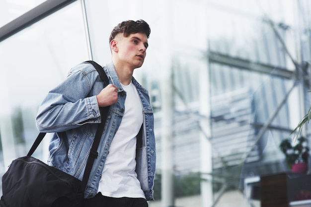 Hombre guapo joven con una bolsa en el hombro a toda prisa hacia el aeropuerto.