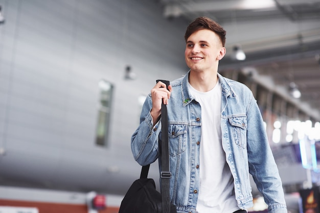 Hombre guapo joven con una bolsa en el hombro a toda prisa hacia el aeropuerto.