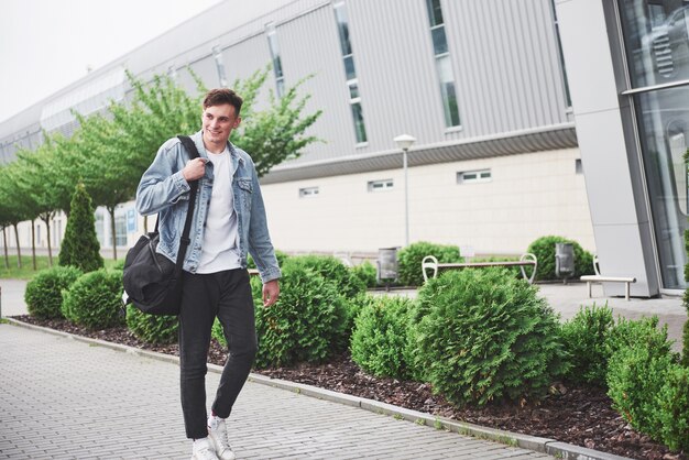 Hombre guapo joven con una bolsa en el hombro a toda prisa hacia el aeropuerto.