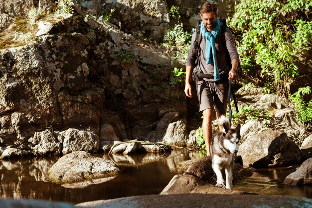 Hombre guapo joven caminando con perros huskies en el cañón cerca del agua