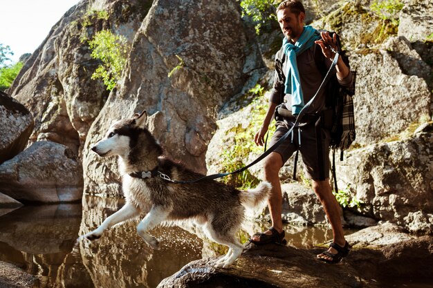 Hombre guapo joven caminando con perros huskies en el cañón cerca del agua