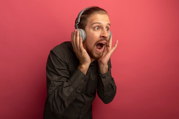 Hombre guapo joven en camisa gris con auriculares en la cabeza mirando a un lado asombrado y sorprendido