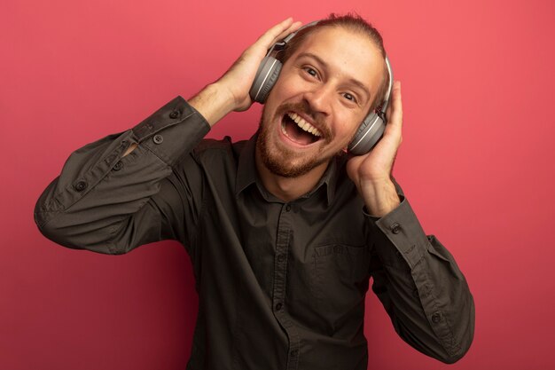 Hombre guapo joven en camisa gris con auriculares en la cabeza sonriendo con cara feliz