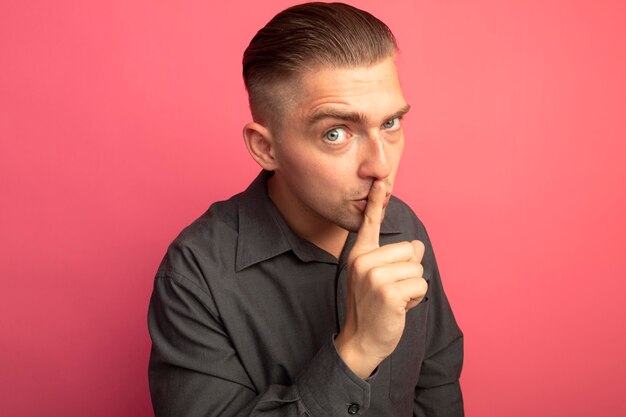 Hombre guapo joven en camisa gris haciendo gesto de silencio con el dedo en los labios