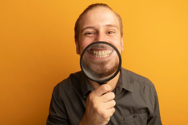 Hombre guapo joven en camisa gris con lupa delante de su gran sonrisa mostrando sus dientes