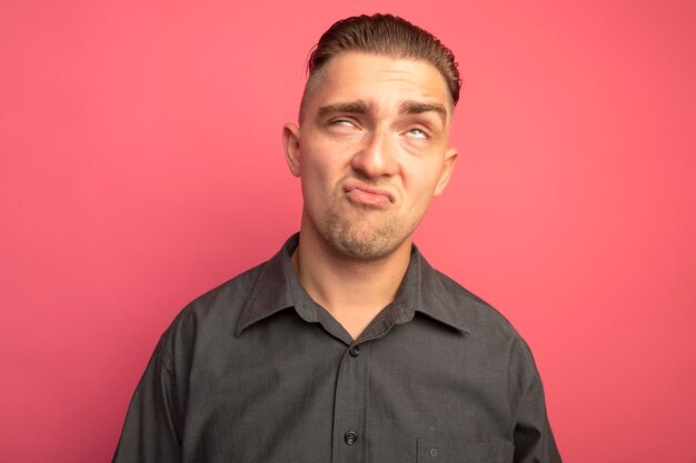 Hombre guapo joven en camisa gris rodando los ojos hacia arriba está molesto y disgustado