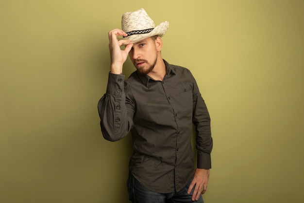 Hombre guapo joven en camisa gris y sombrero de verano con expresión de confianza