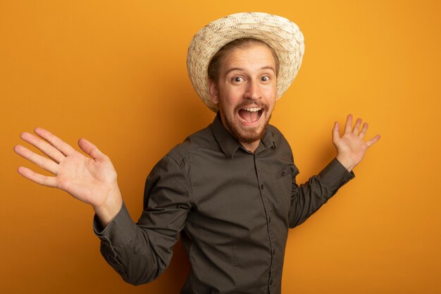 Hombre guapo joven en camisa gris y sombrero de verano feliz y emocionado extendiendo los brazos a los lados