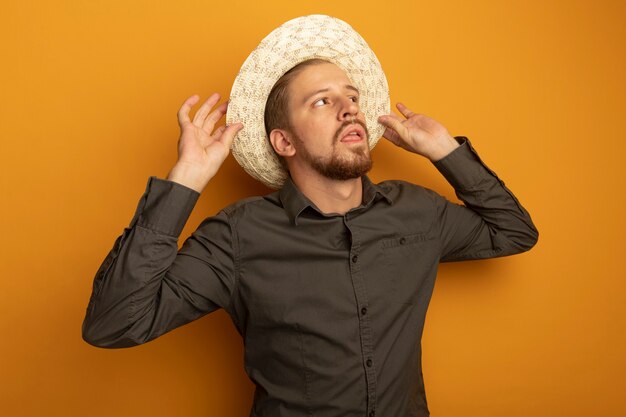 Hombre guapo joven en camisa gris y sombrero de verano mirando a un lado con expresión de confianza