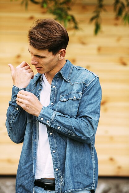 Hombre guapo joven en una camisa de mezclilla posando contra una pared de madera
