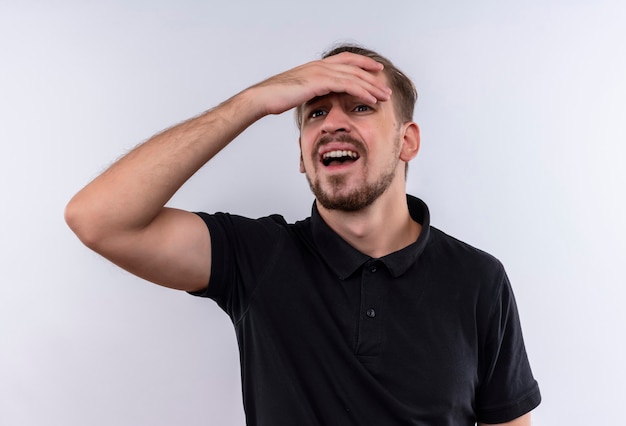 Foto gratuita hombre guapo joven en camisa polo negra mirando confundido y ansioso mirando hacia arriba con la mano en la cabeza de pie sobre fondo blanco