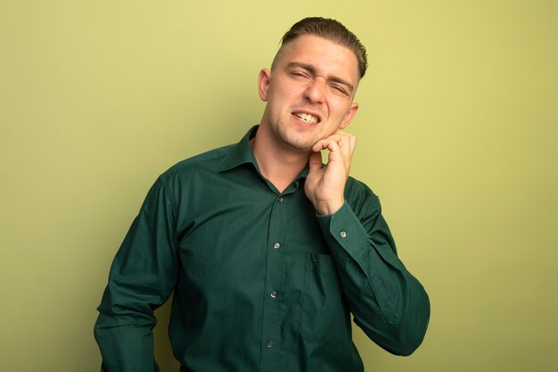 Hombre guapo joven en camisa verde confundido rascándose la cara