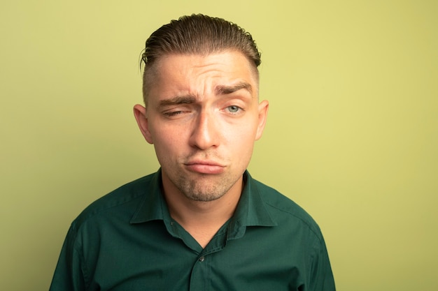 Hombre guapo joven en camisa verde está confundido y disgustado