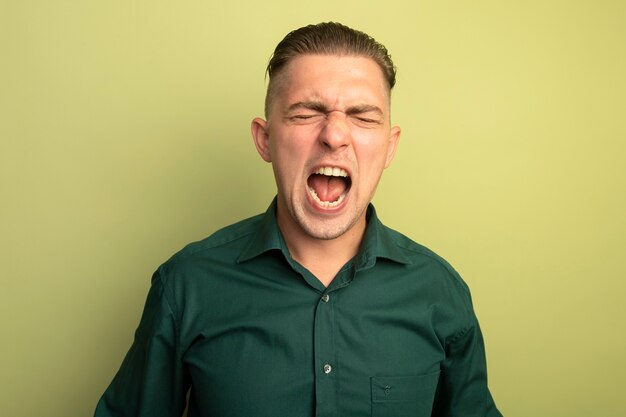 Hombre guapo joven en camisa verde gritando con expresión agresiva irritado y enojado