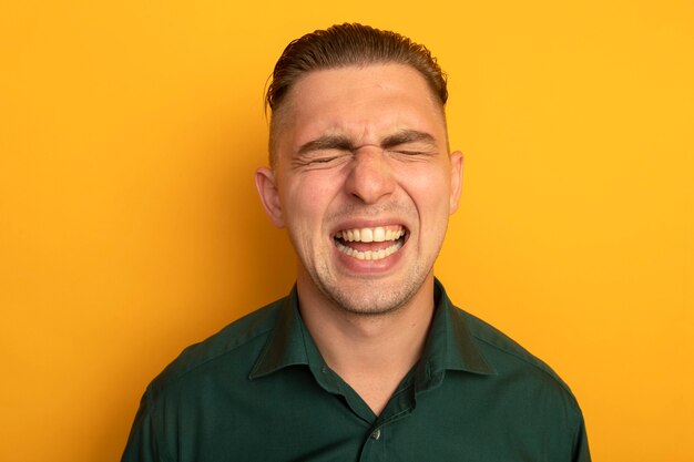 Hombre guapo joven en camisa verde gritando con expresión molesta