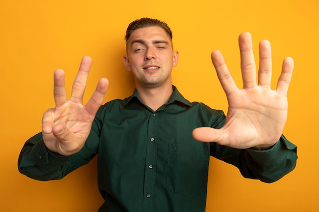 Hombre guapo joven en camisa verde mostrando y apuntando hacia arriba con el dedo número ocho sonriendo confiado