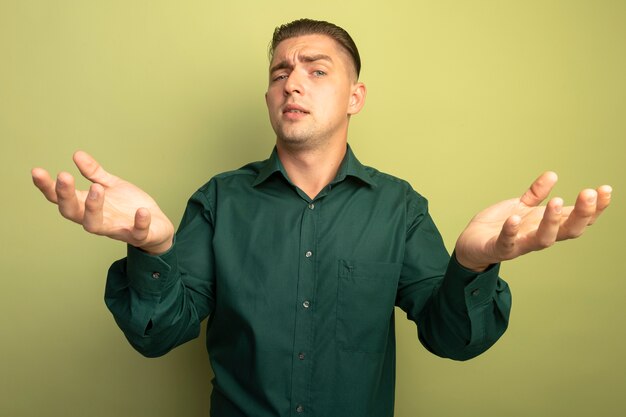 Hombre guapo joven en camisa verde de pie sobre la pared de luz