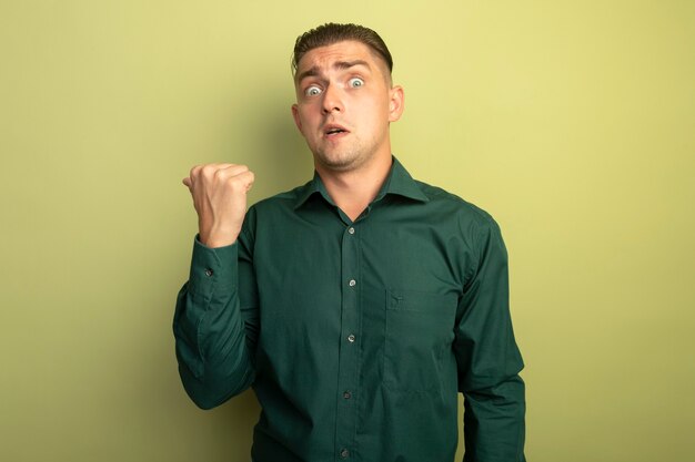 Hombre guapo joven en camisa verde preocupado y asustado levantando el puño