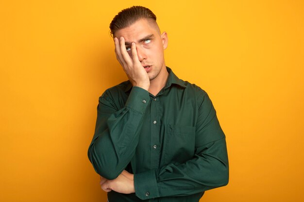 Hombre guapo joven en camisa verde rodando los ojos hacia arriba cansado y molesto