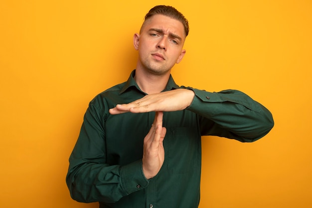 Hombre guapo joven en camisa verde con rostro serio haciendo gesto de tiempo con las manos