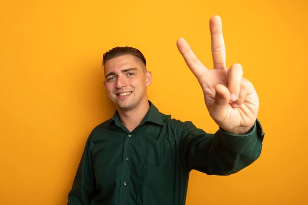 Hombre guapo joven en camisa verde sonriendo alegremente mostrando signo v feliz y positivo