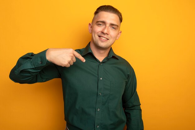 Foto gratuita hombre guapo joven en camisa verde sonriendo confiado apuntando a sí mismo