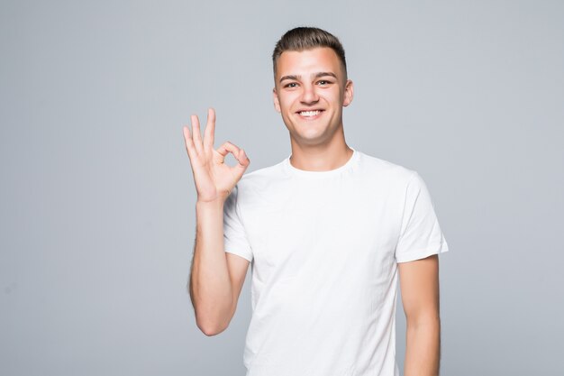 Hombre guapo joven en una camiseta blanca aislada en blanco muestra signo de ok