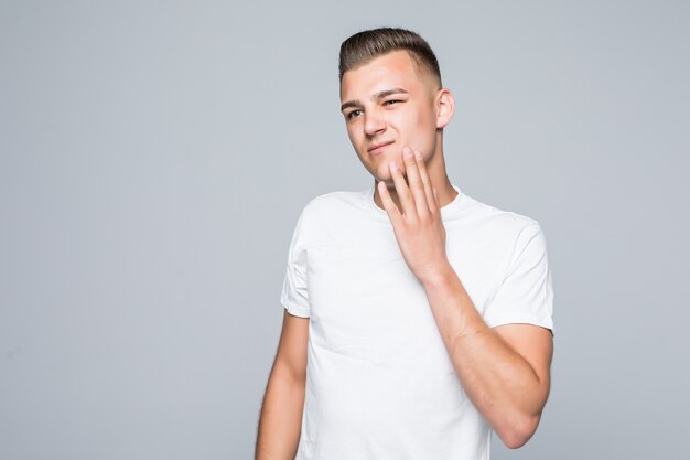 Hombre guapo joven con una camiseta blanca aislado en blanco está tocando su rostro