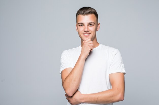 Hombre guapo joven en una camiseta blanca aislado en blanco mantenga el brazo debajo de la barbilla