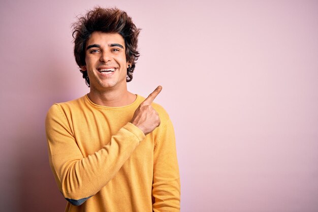 Hombre guapo joven con camiseta casual amarilla de pie sobre fondo rosa aislado alegre