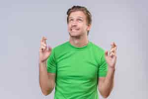 Foto gratuita hombre guapo joven con camiseta verde haciendo deseo deseable cruzando la mano con expresión esperanzada