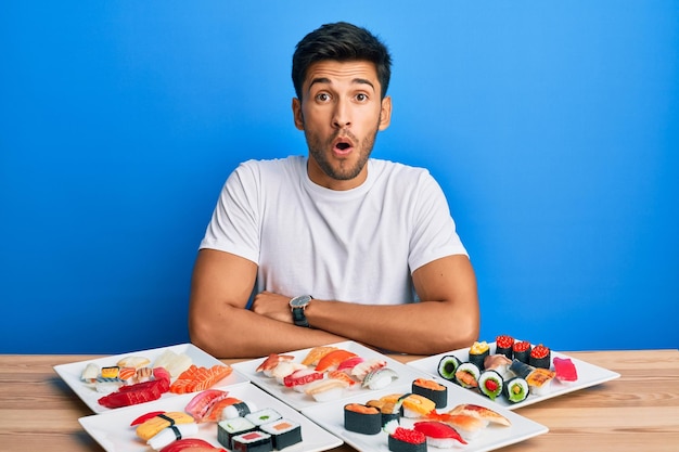 Hombre guapo joven comiendo sushi sentado en la mesa asustado y conmocionado con expresión de sorpresa miedo y cara emocionada