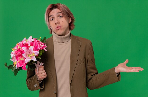 Hombre guapo joven confundido sosteniendo un ramo de flores y manteniendo su mano abierta