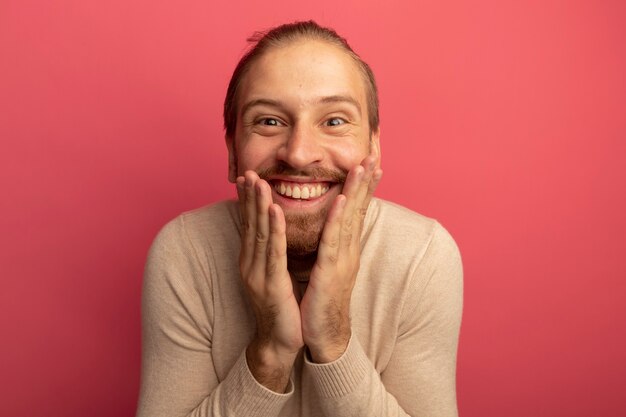 Hombre guapo joven en cuello alto beige feliz y sorprendido sonriendo ampliamente