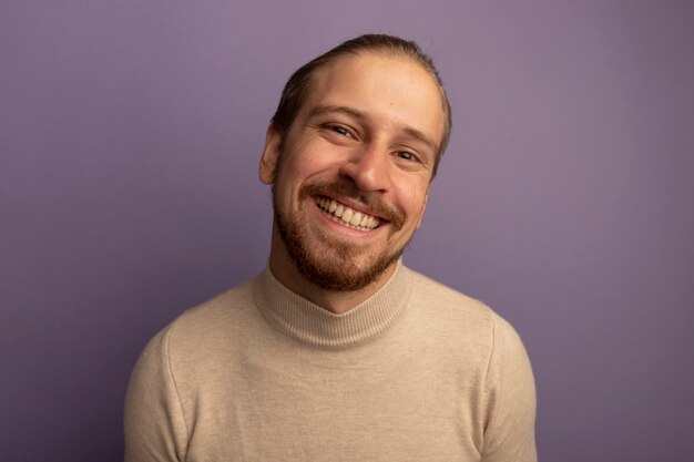 Hombre guapo joven en cuello alto beige sonriendo mostrando los dientes