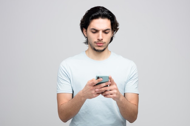 Hombre guapo joven disgustado usando su teléfono móvil aislado sobre fondo blanco.