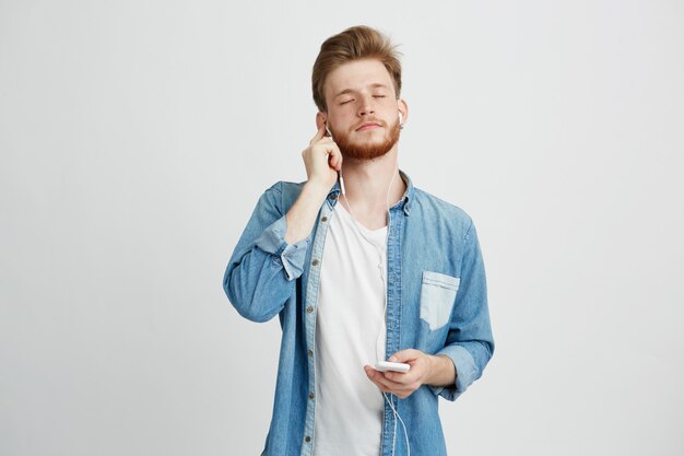 Hombre guapo joven escuchando música en streaming en auriculares con los ojos cerrados disfrutando.