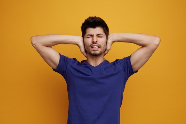 Hombre guapo joven estresado cerrando los oídos con las manos con los ojos cerrados sobre fondo amarillo