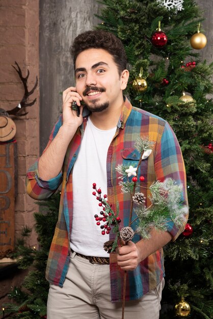 Hombre guapo joven hablando con el teléfono delante del árbol de Navidad.